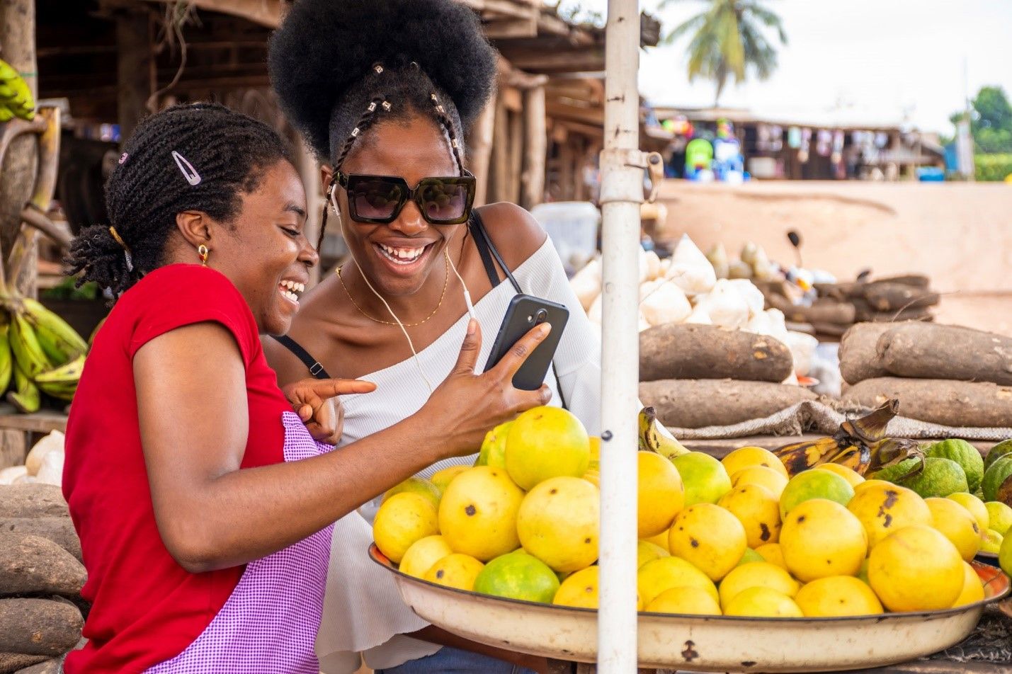 Two women at an African market stall smiling at a smartphone
